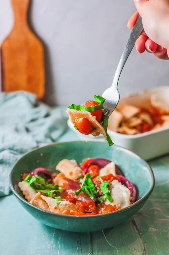 forkful of spinach ravioli with roasted tomatoes and basil in a blue bowl