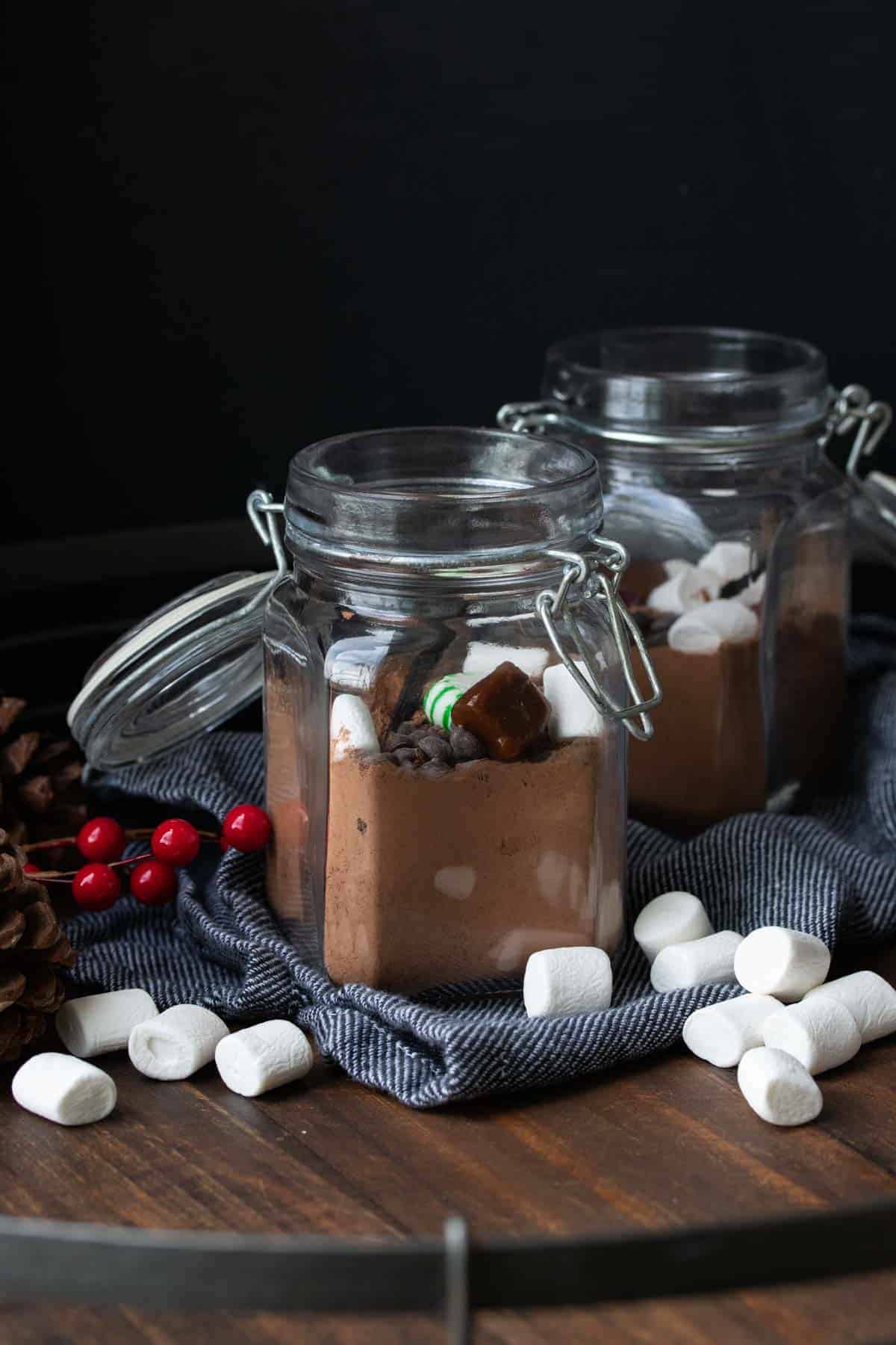 Two glass jars on a wooden tray filled with hot chocolate mix.