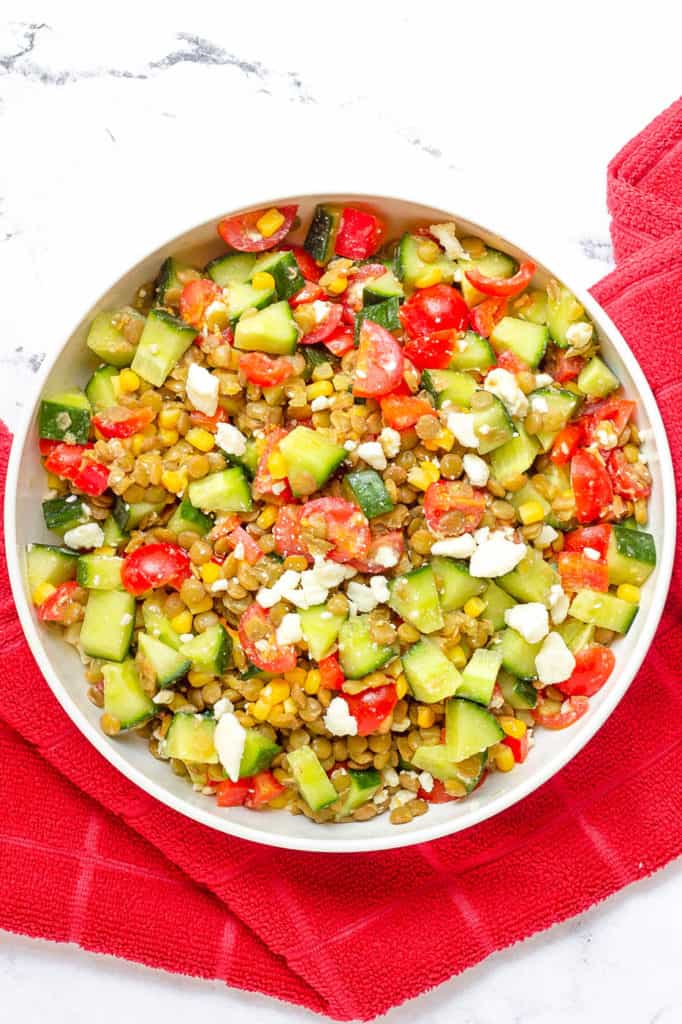 feta salad with lentils, cucumbers, tomatoes, corn in a white bowl