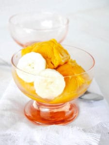 mango nice cream in a glass container with sliced bananas