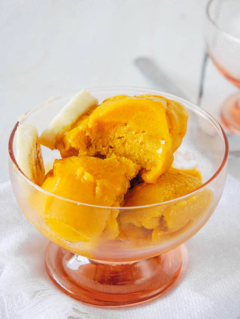 mango nice cream in a glass container with sliced bananas