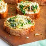 mushroom toast with spinach and roasted garlic on a wooden cutting board