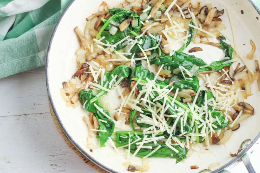 parmesan cheese added to spinach and mushrooms in a pan