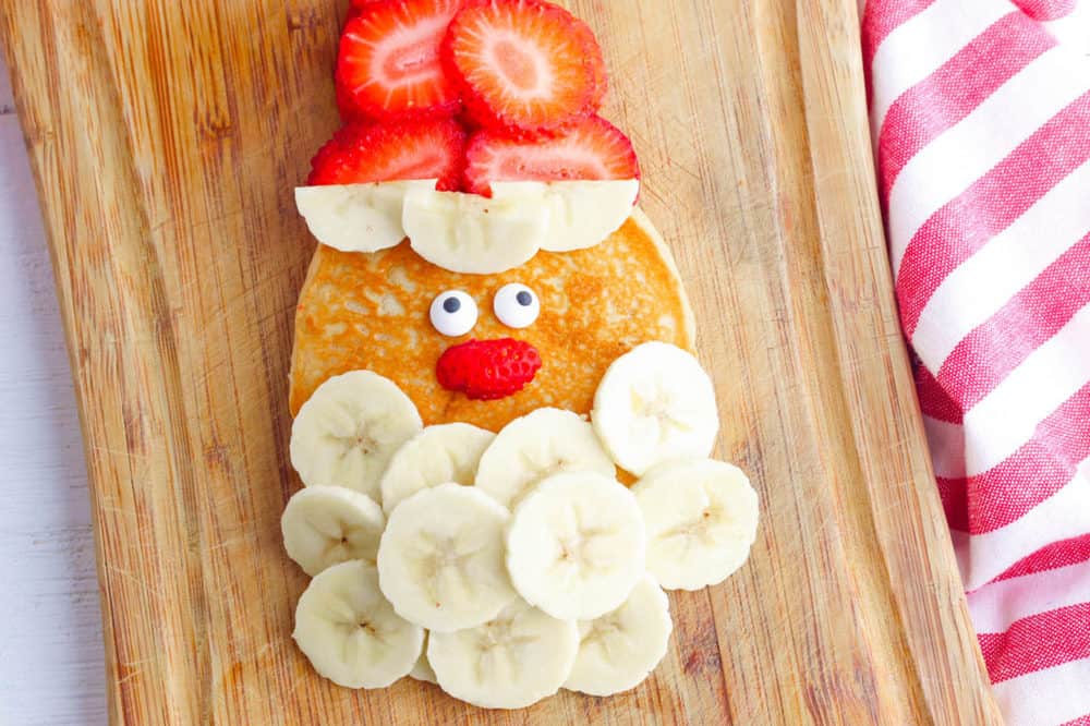 santa pancakes - christmas and holiday breakfast - made with bananas for a beard, strawberries for a hat, and candy eyes on top of a homemade pancake