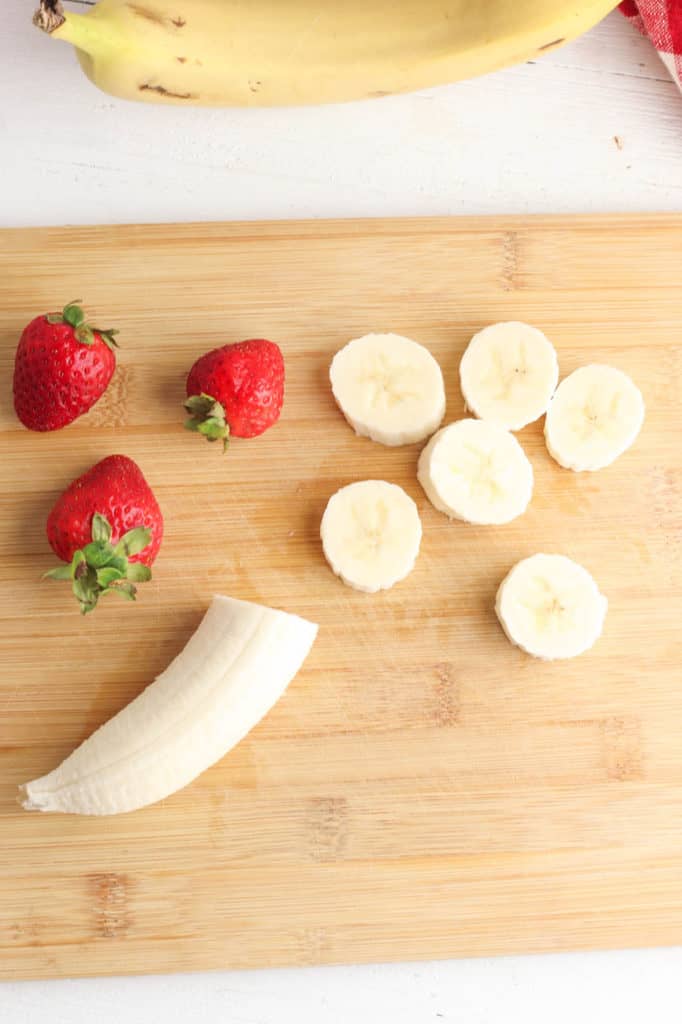 cut strawberries and banana on a cutting board