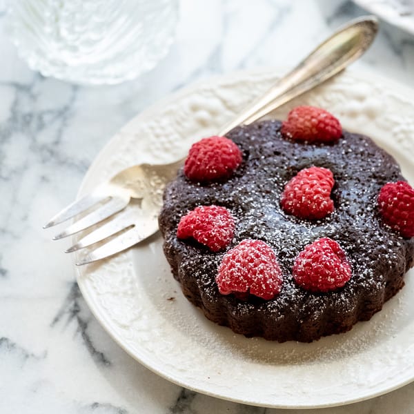 brownie tart topped with fresh raspberries on white plate with fork