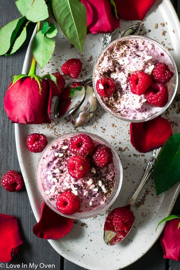 overhead of chocolate raspberry mousse cups on platter covered with roses and rose petals