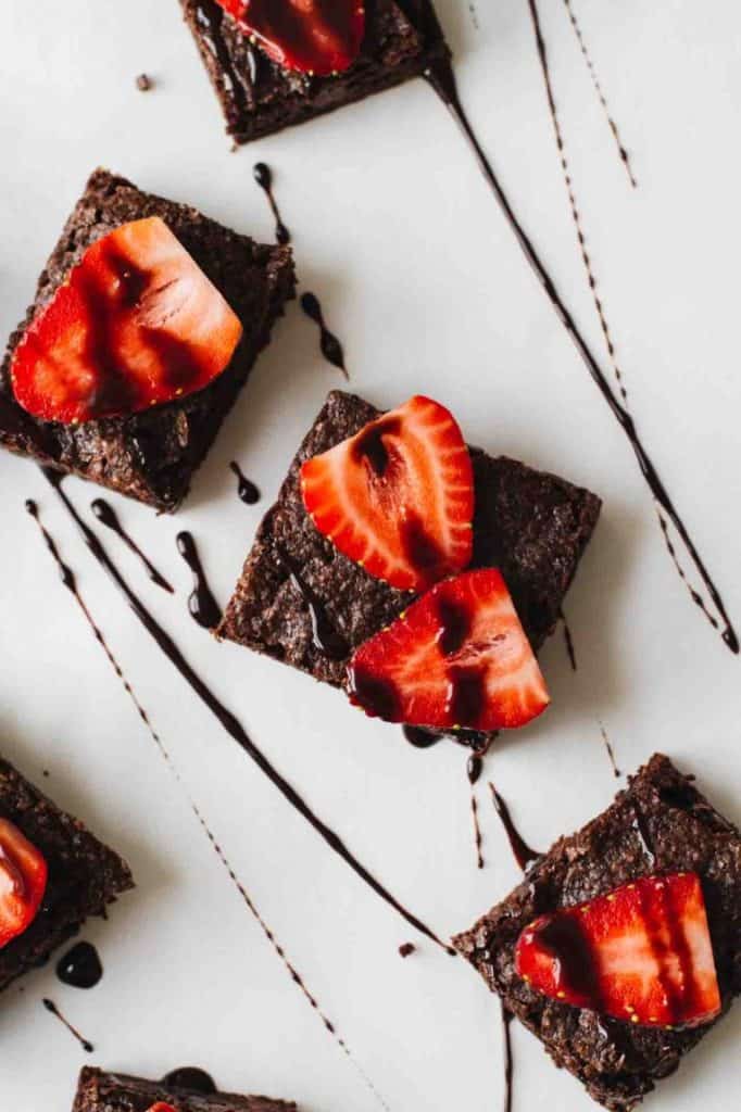 brownie squares topped with sliced strawberries and drizzled with chocolate sauce on white plate