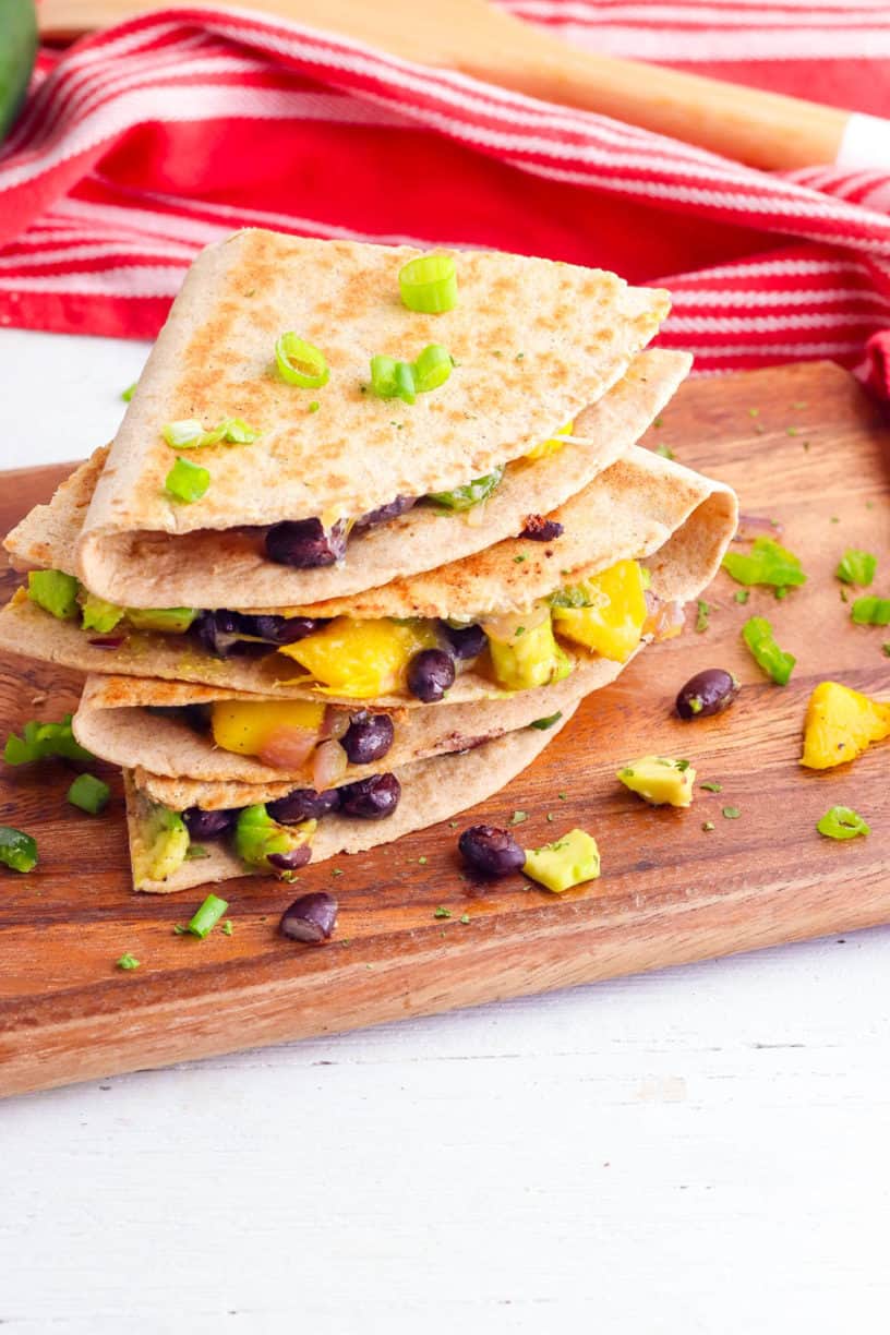 avocado quesadillas with poblanos mangos and black beans stacked on a wooden cutting board