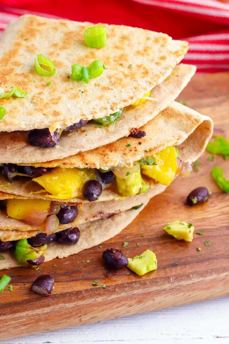 avocado quesadillas with poblanos mangos and black beans stacked on a wooden cutting board