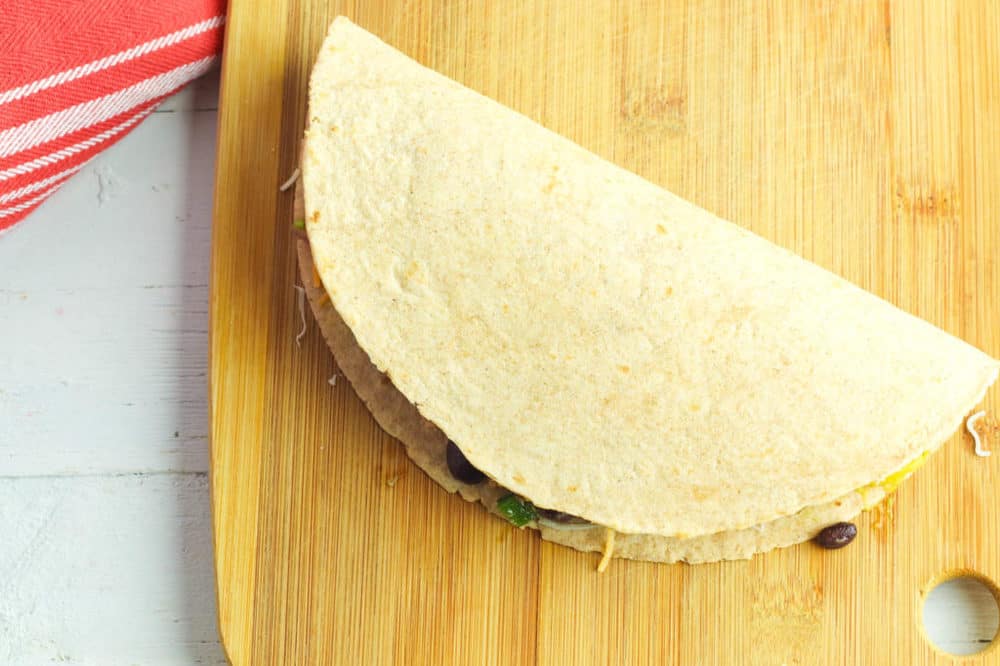 tortilla stuffed with filling folded on a wooden cutting board
