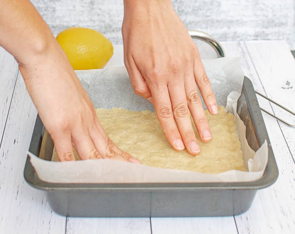 almond crust being pressed into a pan