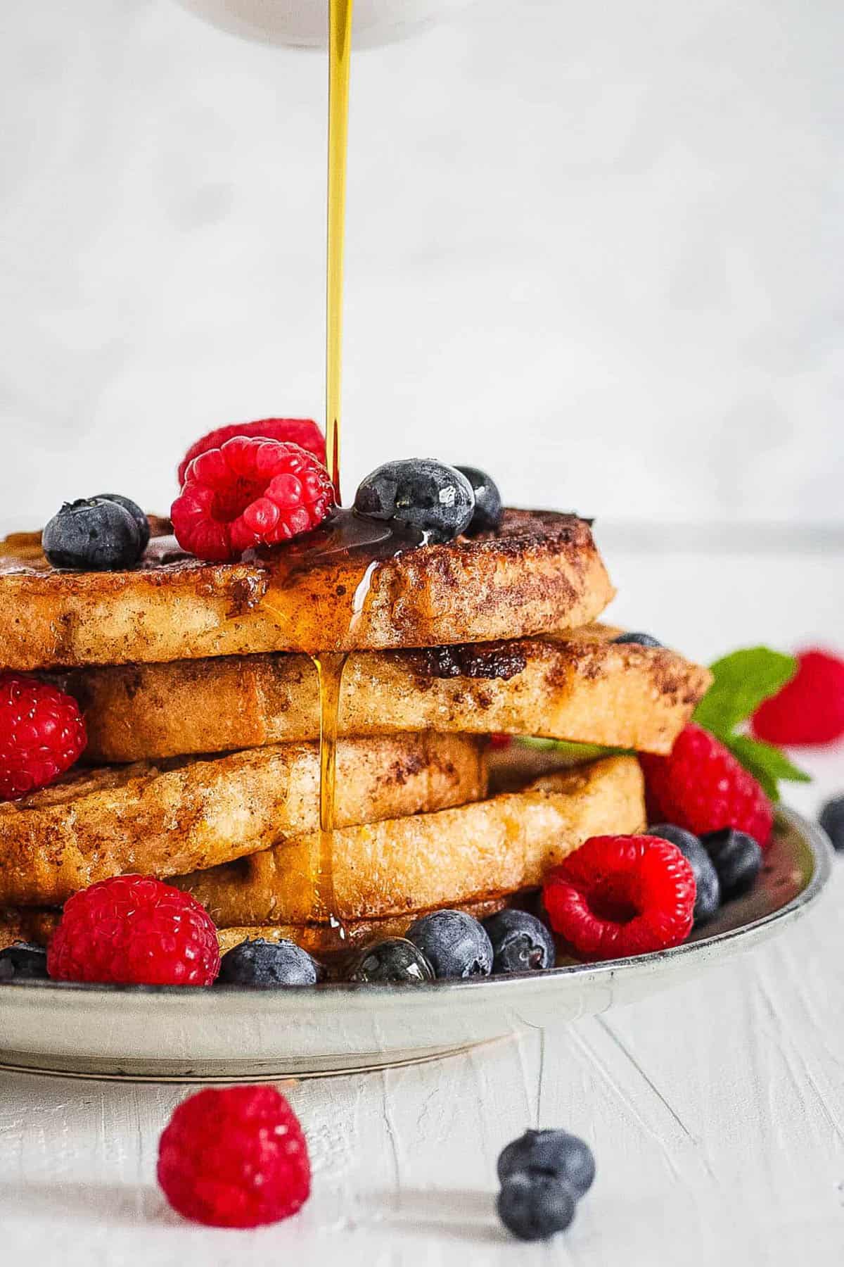 Healthy french toast, served on a white plate with fresh berries and maple syrup.