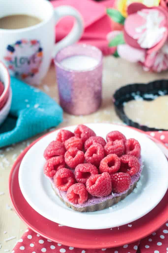 raspberry cheesecake tart in the shape of a heart topped with fresh raspberries