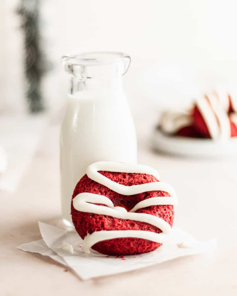 red velvet donut with vanilla icing propped up next to to a small jug of milk