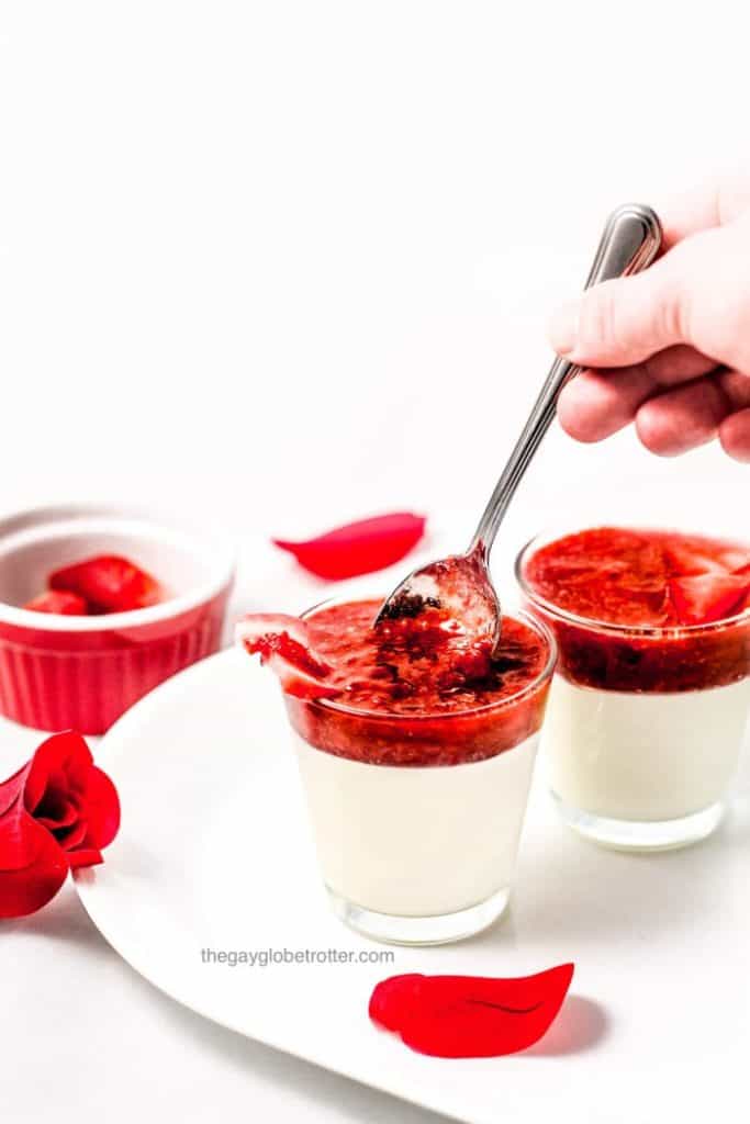 strawberry panna cottas with layer of white and red, on white plate with hand dipping spoon inside