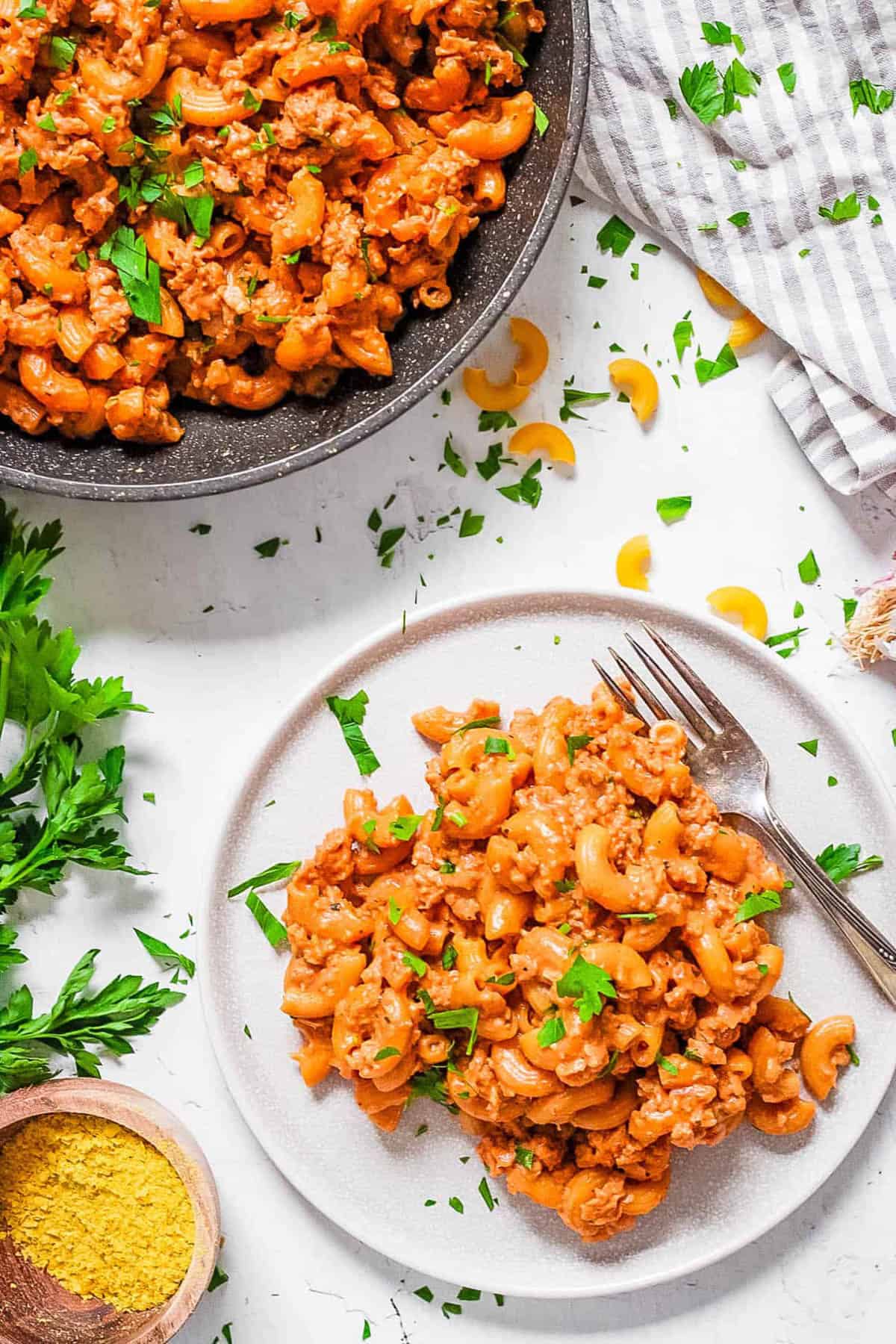 Vegan hamburger helper served on a white plate with a fork and fresh herbs as a garnish.