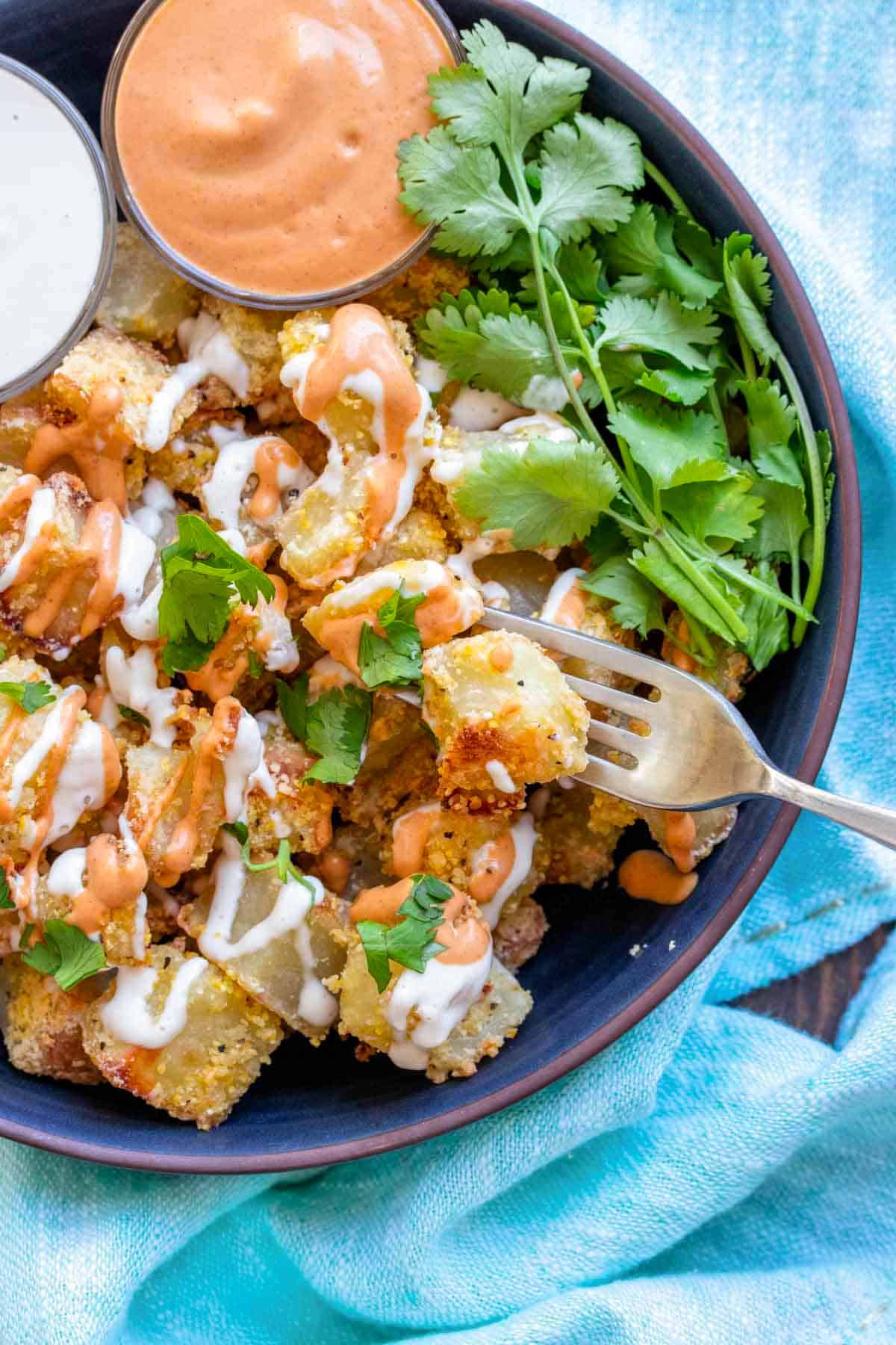 Vegan patatas bravas served on a gray plate with a drizzle of paprika sauce and garlic aioli and a garnish of parsley.