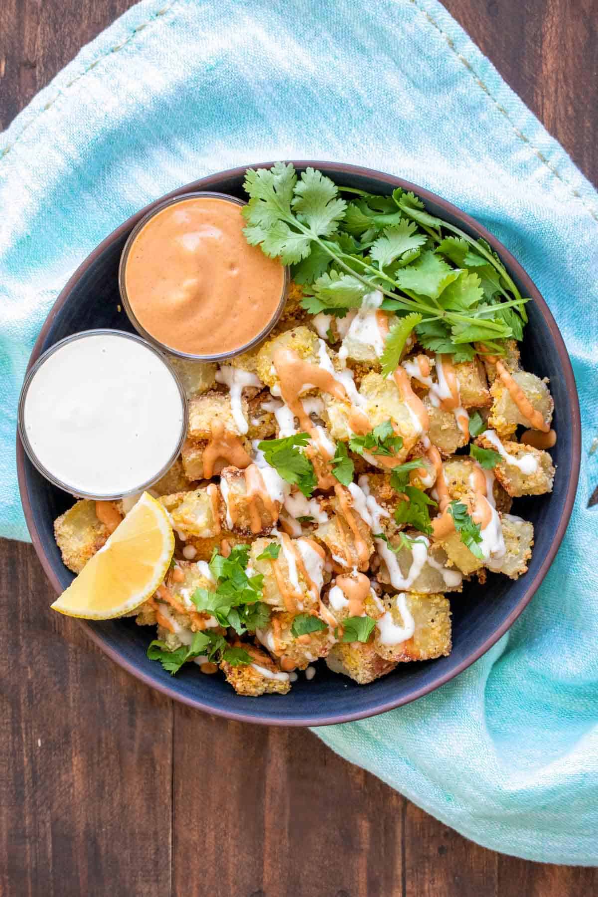 Vegan patatas bravas in a dark blue bowl, drizzled with sauce.