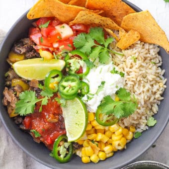 vegetarian burrito bowl with black beans, tortilla chips, corn, cheese and lime