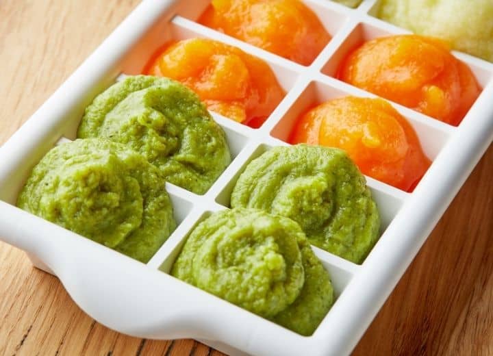 pureed food in ice tray including green peas, orange carrots, and yellow banana puree 