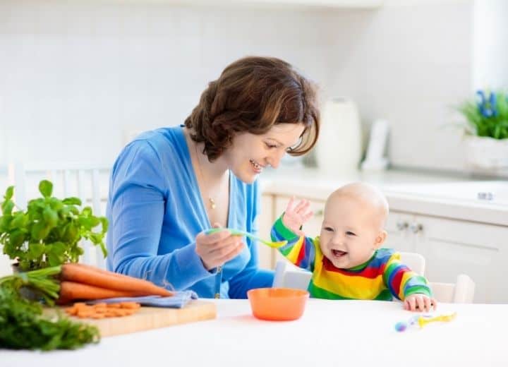 mom feeding happy baby pureed food from orange bowl