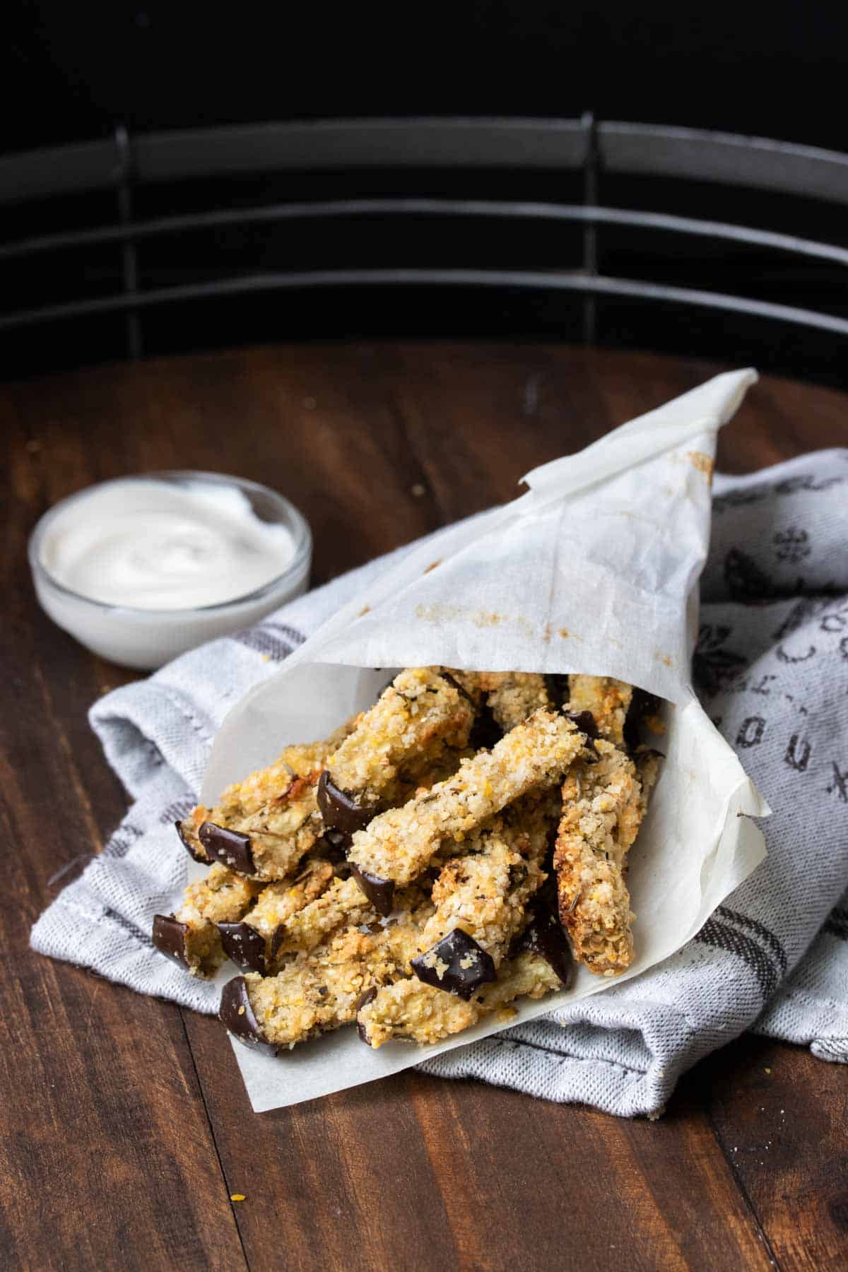 A cone of parchment paper with eggplant fries inside on a wooden surface