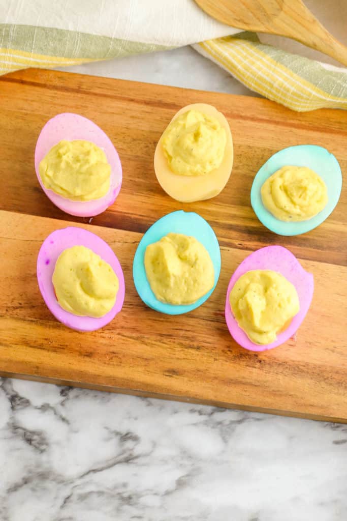 healthy deviled eggs dyed in pastel colors on a wooden cutting board