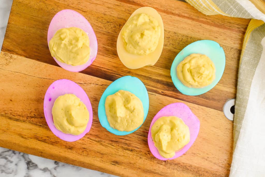 healthy deviled eggs dyed in pastel colors on a wooden cutting board