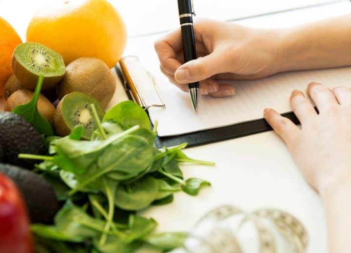 woman writing on notepad beside fresh produce - meal planning template