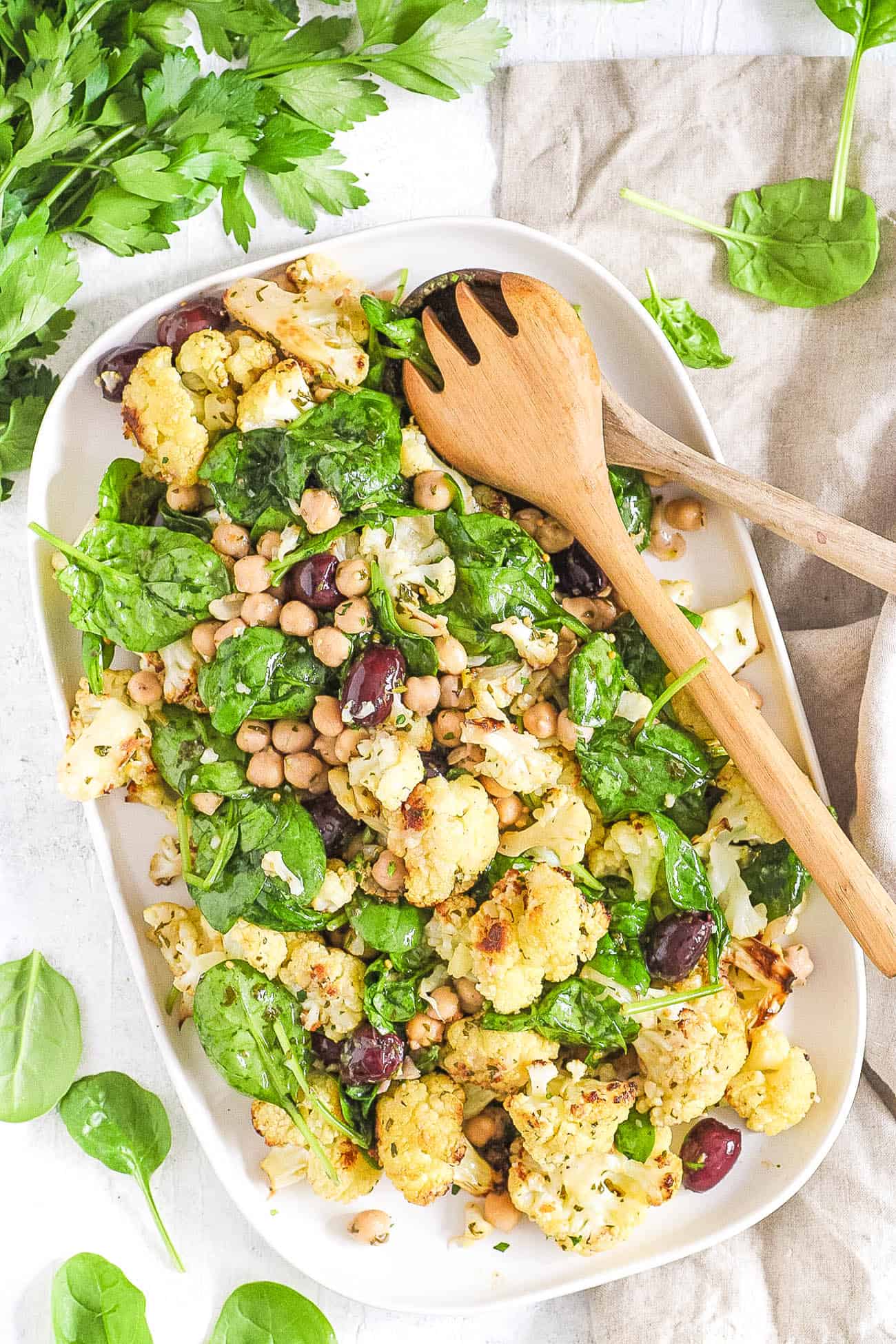 roasted cauliflower salad with spinach and chickpeas and kalamata olives, served on a white plate