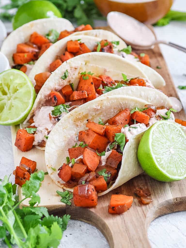 sweet potato tacos with lots of taco toppings - black beans and a spicy yogurt sauce served on a wooden cutting board