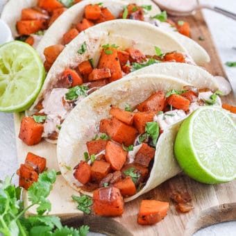 sweet potato tacos with black beans and a spicy yogurt sauce served on a wooden cutting board