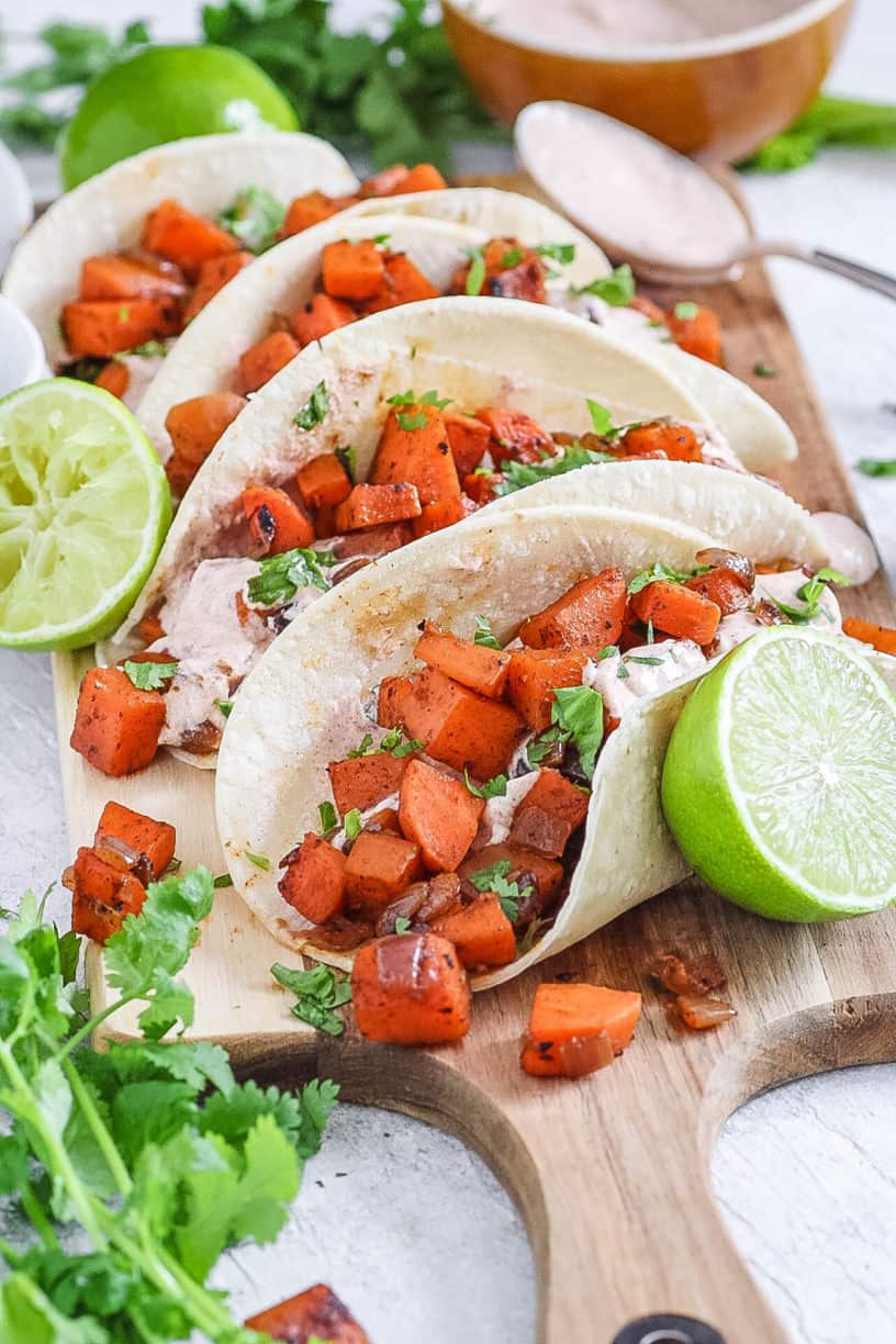 sweet potato tacos with black beans and a spicy yogurt sauce served on a wooden cutting board