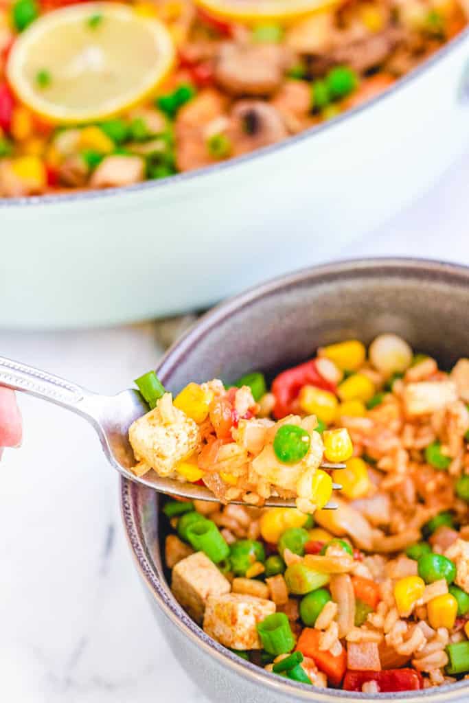 single serving of vegan paella with tofu with a skillet of paella in the background