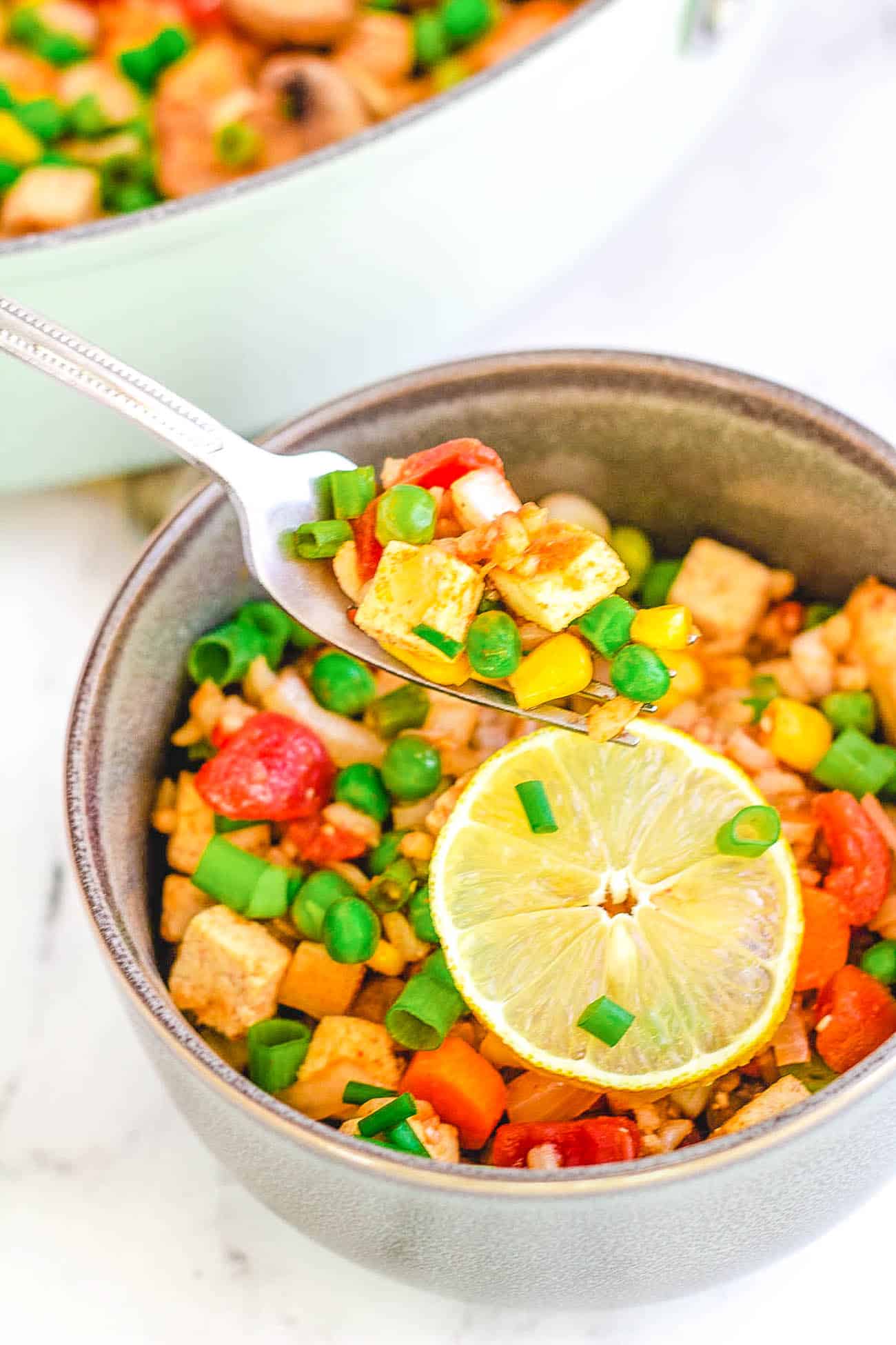 single serving of vegan paella with tofu with a skillet of paella in the background