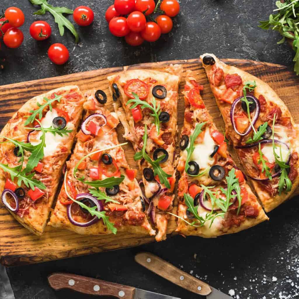 Pizza garnished with healthy pizza toppings like veggies and fresh arugula, served on a wooden pizza board, top view.