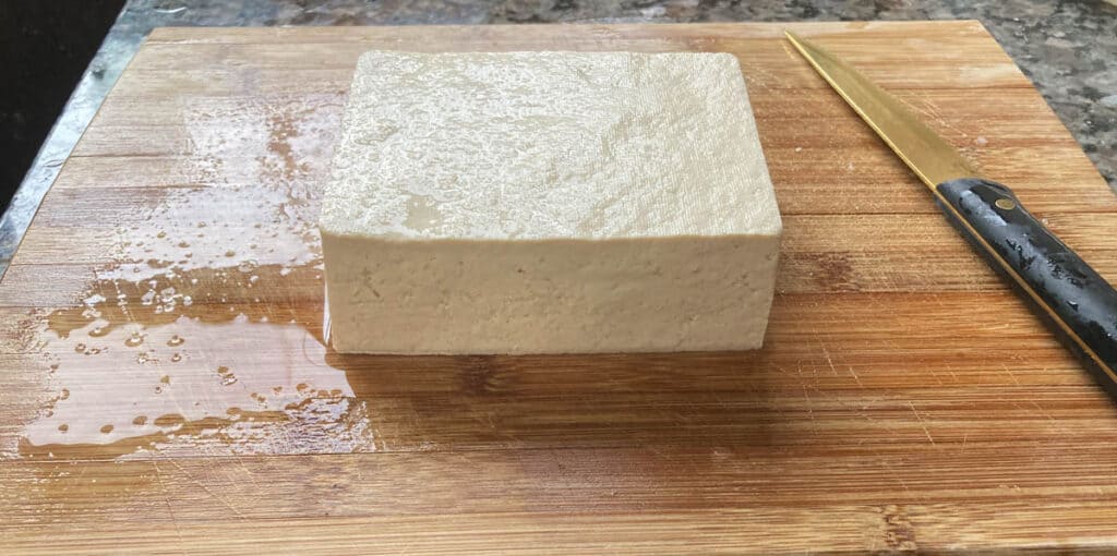Block of tofu on a cutting board.