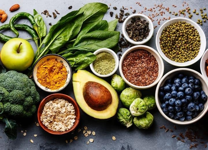 assorted healthy foods in small bowls: broccoli, apple, basil, hot pepper, avocado, brussel sprouts, flax seeds, blueberries - all ingredients on a vegetarian grocery list