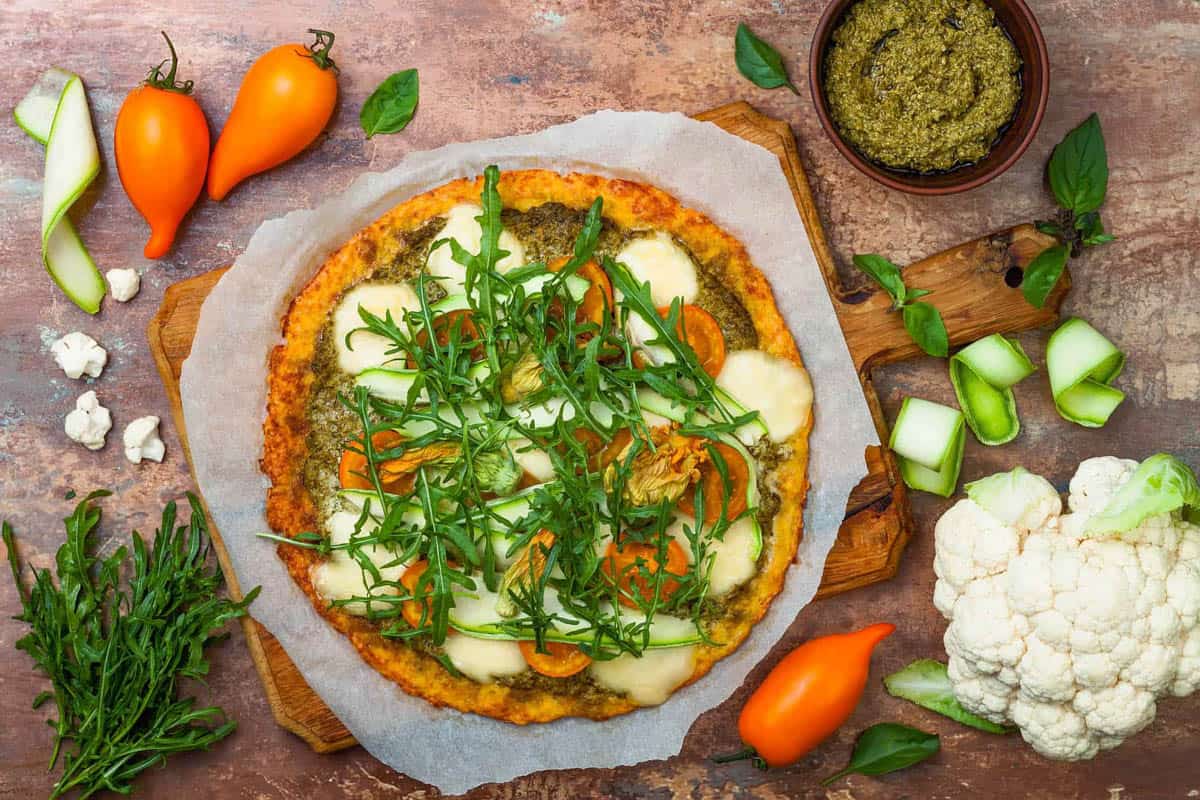 Pizza garnished with healthy pizza toppings like veggies and fresh greens, served on a wooden pizza board, top view.