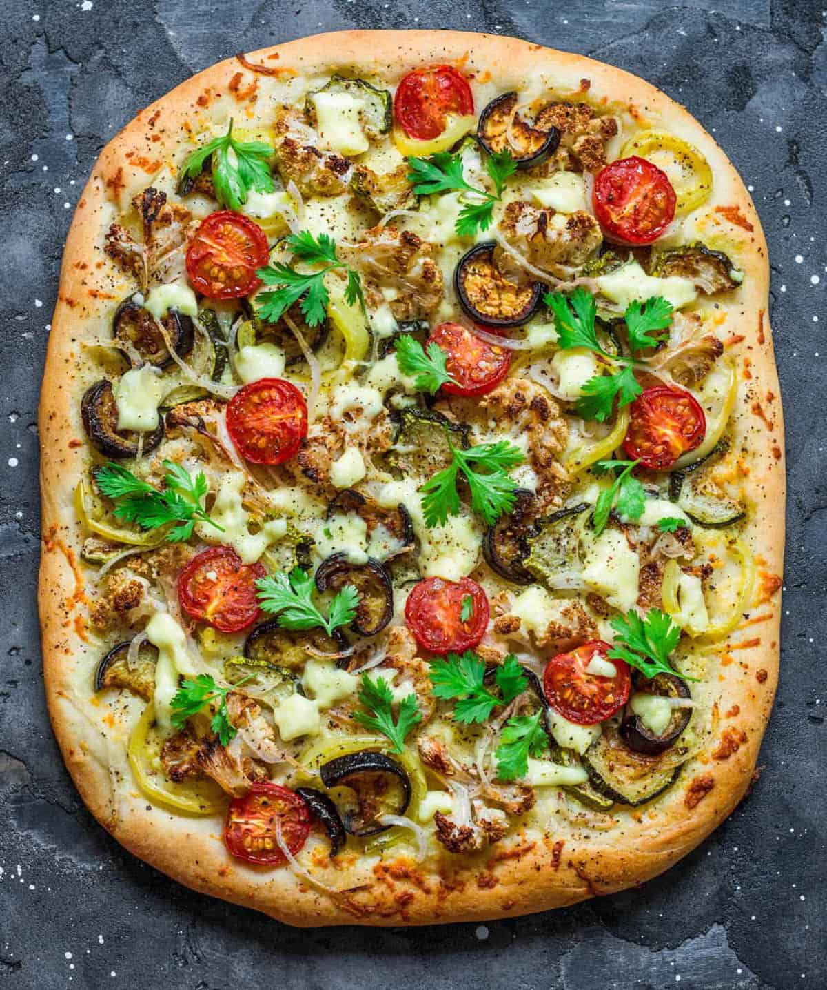 Pizza garnished with low calorie, healthy pizza toppings like veggies and fresh herbs, served on a grey countertop, top view.