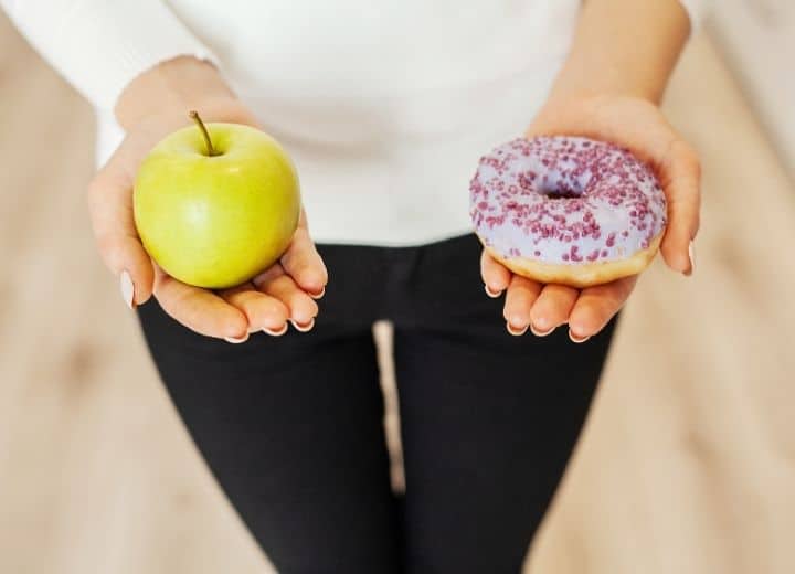 woman holding in apple in one hand and a donut in the other hand