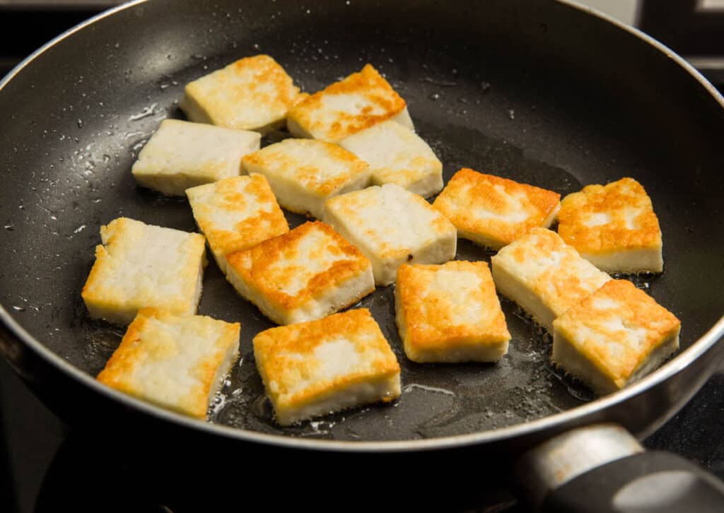 Tofu cubes being pan fried in a pan.