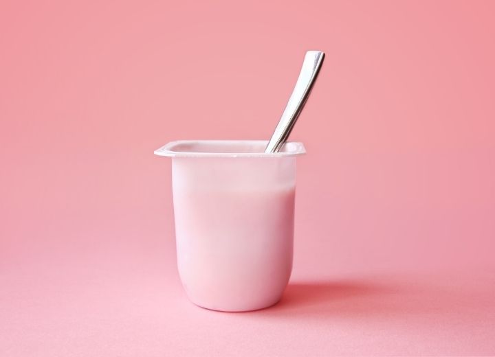 pink strawberry yogurt in plastic yogurt cup with spoon on pink background