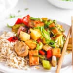 sweet and sour tofu with veggies, served on a white plate with chopsticks