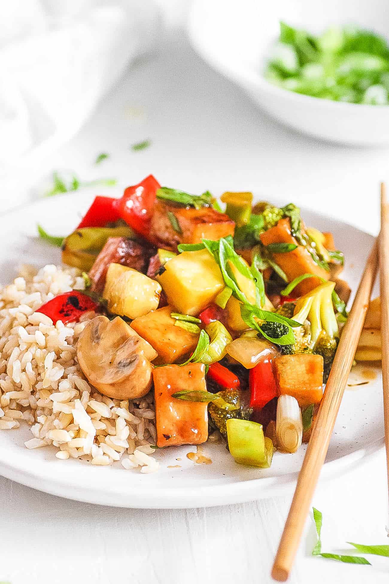 sweet and sour tofu with veggies, served on a white plate with c،psticks