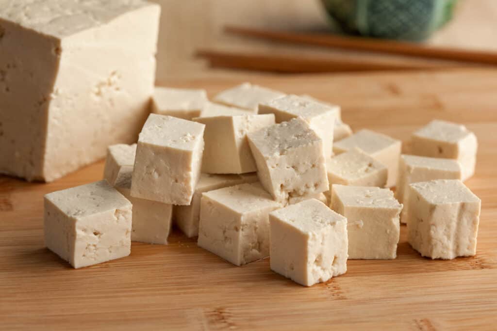 Tofu cut into cubes, on a wooden cutting board.