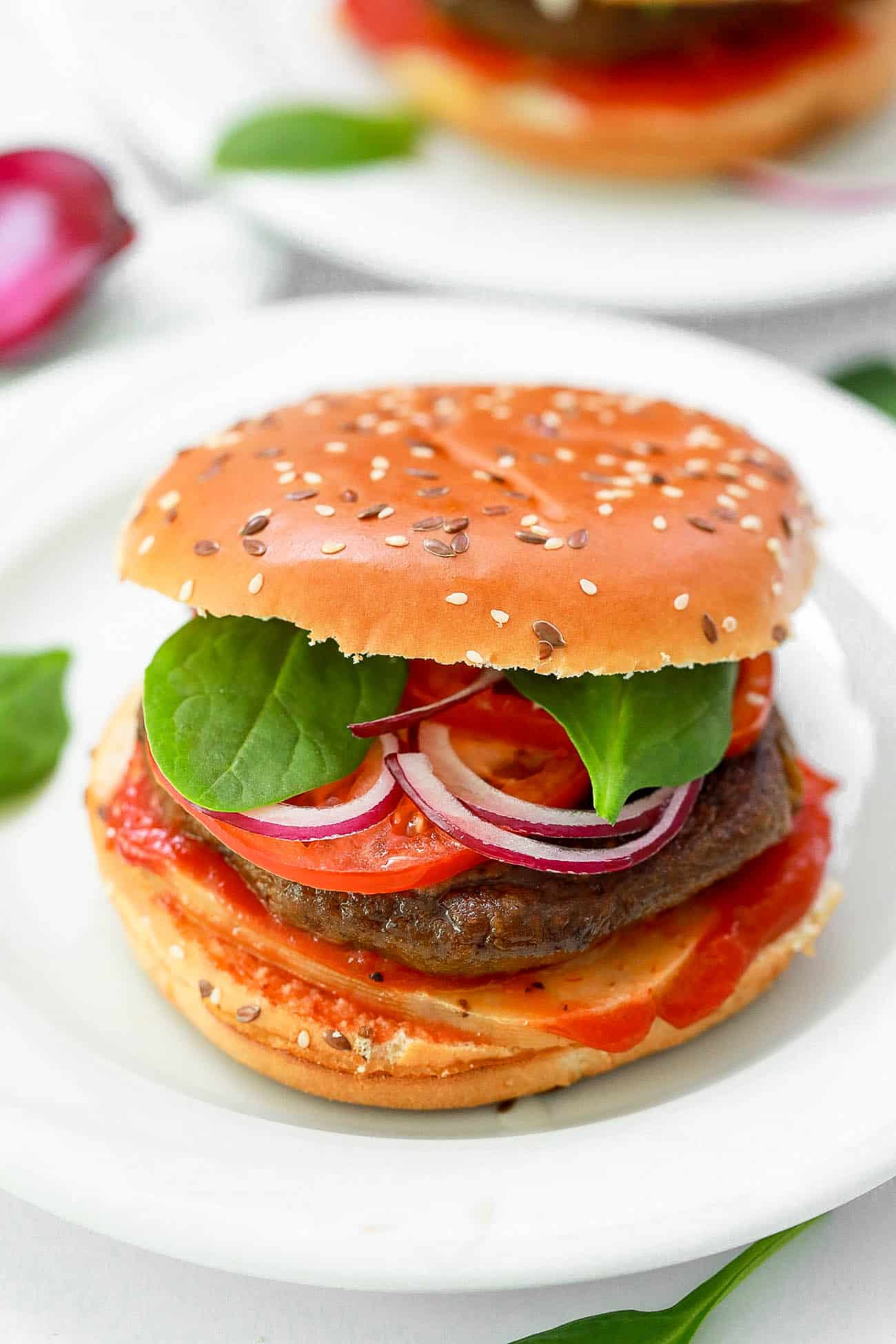 high protein veggie burgers on a white plate - black bean pumpkin burgers topped with spinach, tomato, cheese, onions, ketchup