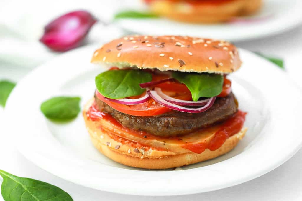 pumpkin burgers on a white plate - black bean pumpkin burgers topped with spinach, tomato, cheese, onions, ketchup