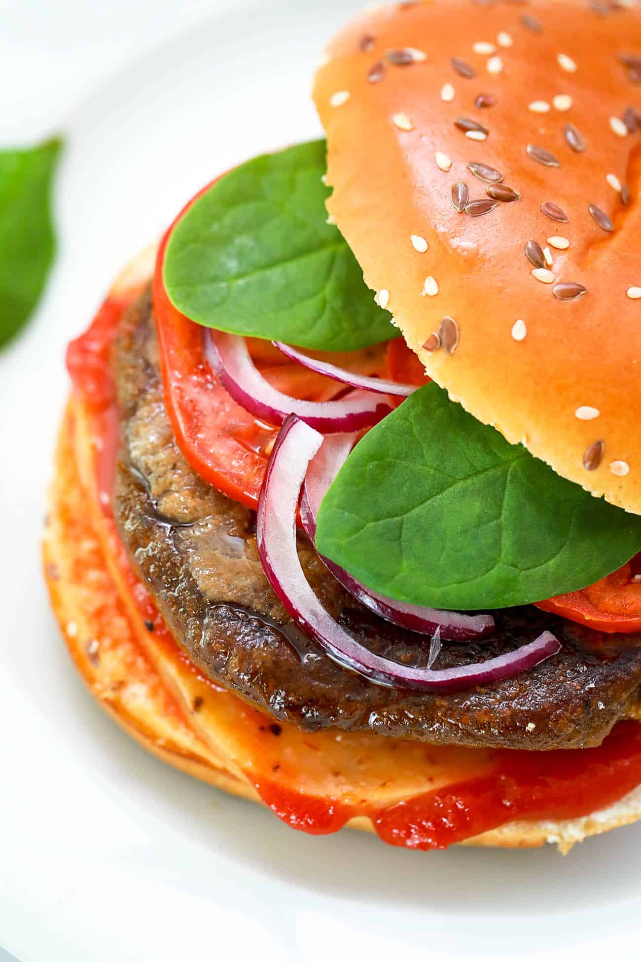 pumpkin burgers on a white plate - black bean pumpkin burgers topped with spinach, tomato, cheese, onions, ketchup